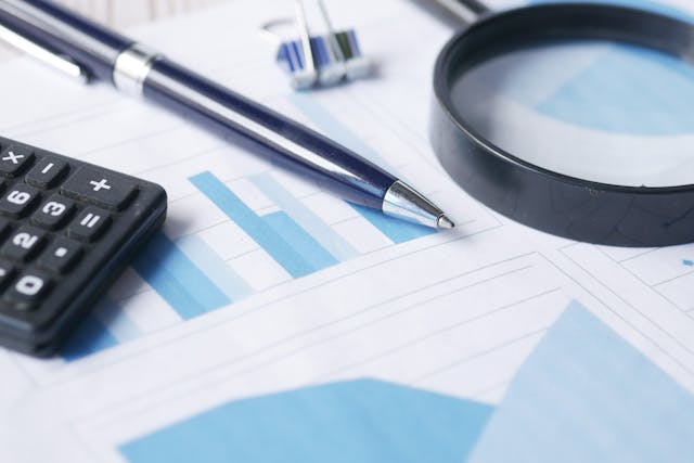 a calculator, magnifying glass and a pen on a bunch of graphs