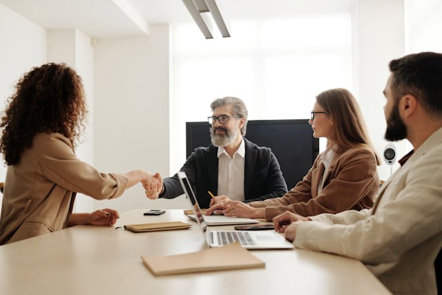 four people in a conference room as two of them shake hands